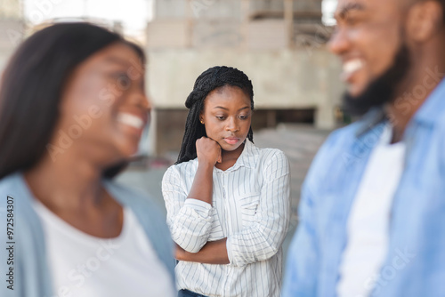 Third wheel. Upset black girl jealous to her dating friends, standing alone on background outdoors, selective focus