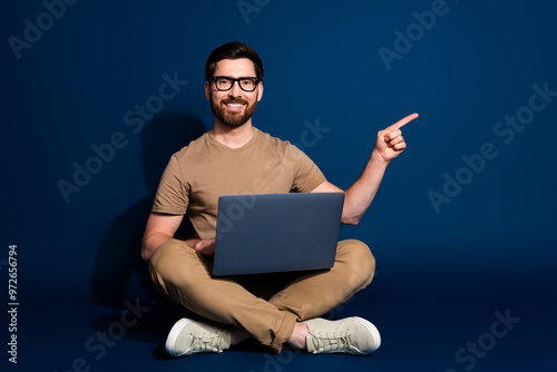 Photo of engineer brunet man sitting with laptop working directing finger empty space new technology isolated on dark blue color background