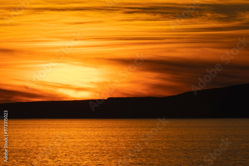 Golden sunset over Isle of Arran in the Firth of Clyde sea with band of dark cloud in sky