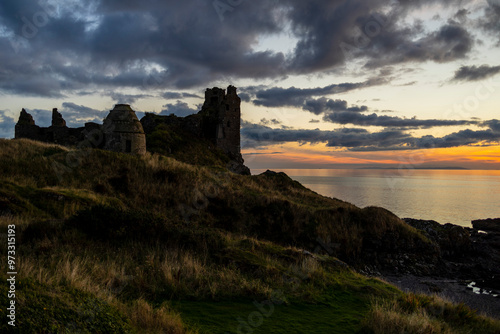 Dunure Castle and Dovecot ruins at sunset beside Firth of Clyde sea with grass and rocky shore