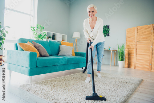 Photo of charming senior woman dressed casual cardigan use modern vacuum cleaner cleaning home house apartment room indoors