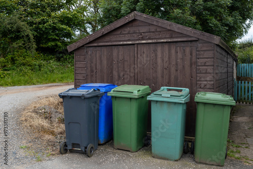 UK waste wheelie wheeled bins in row stored in front of brown wooden garage