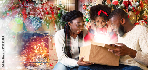 Magical Christmas. Excited african american family of three opening shining gift box in living room near Xmas tree, celebrating holidays at home