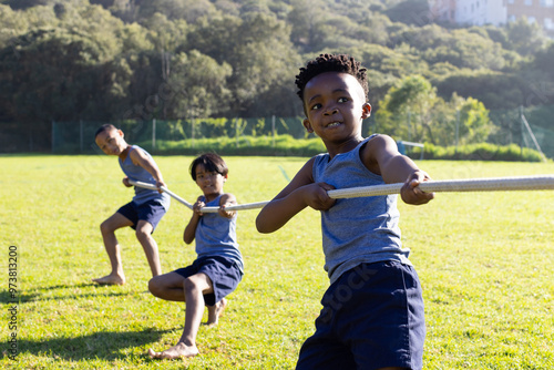 Playing tug of war, multiracial boys enjoying outdoor activity at school field