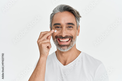 Happy middle aged 45 years old man applying facial anti age skincare cream on face isolated on white background. Smiling mature handsome gray-haired male model advertising skin care product. Portrait.