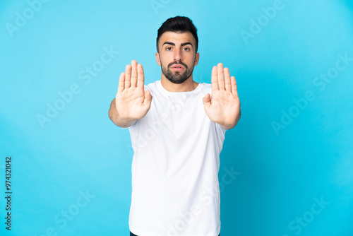 Caucasian man over isolated blue background making stop gesture and disappointed