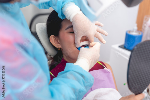 A dental professional applying a fluoride gel tray to a patient's teeth. The patient sits in the dental chair, holding a mirror while the dentist wears gloves and protective clothing.