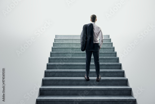 Businessman standing at the base of a concrete staircase, looking up.