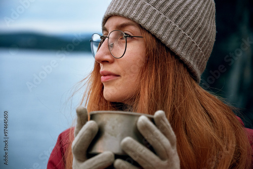 Pretty smiling female traveler drinking from thermos outdoors