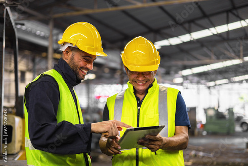 Two men in yellow safety vests are looking at a tablet