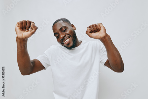 Happy young man celebrating in a bright white t shirt, expressing joy and positivity against a light grey background, embodying success and enthusiasm