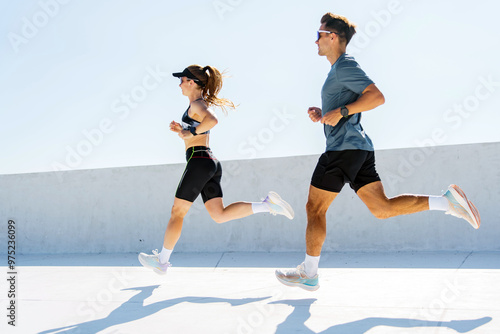 A man and woman are seen running outdoors under bright sunlight, their shadows cast long on the ground.