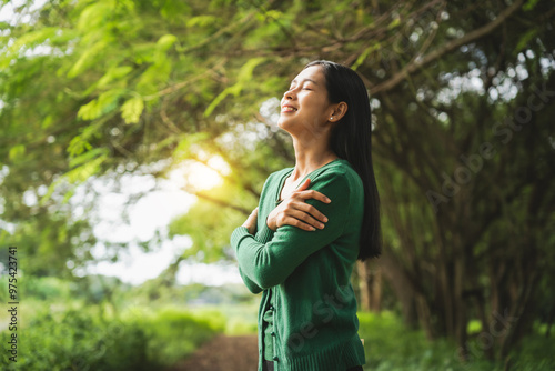 confident asian woman embraces self-love, standing peacefully in serene park at sunset. joyful smile, she enjoys fresh air, breathing deeply, radiates calm and positivity in tranquil surroundings.