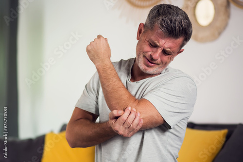 Man With Pain In Elbow. Pain relief concept. Middle age man feeling the pain in hand elbow at home. Male touching his painful elbow