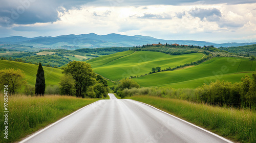 A serene countryside road with lush green hills and distant mountains under a partly cloudy sky.