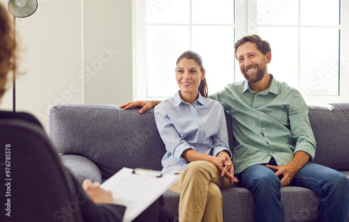 Young smiling couple sitting on sofa and talking with psychologist trying to find problems and solution at counselor's office. Family therapy, relationship and mental health concept.