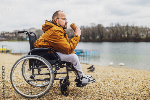 Paraplegic handicapped man in wheelchair is enjoying outdoor and drinking coffee.