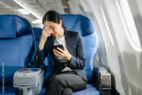 Photo of a frustrated woman sitting on an airplane with her head in her hands. Asian woman sitting