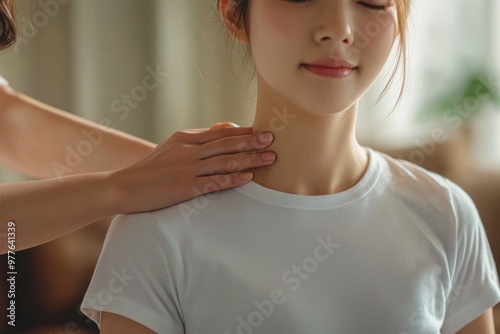 Japanese woman in casual clothes is receiving a neck massage from a physical therapist for chronic stiff neck, with the physical therapist's hands lightly holding her shoulders.