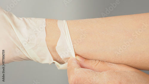 Hand Wearing torn or leak latex glove on gray background.