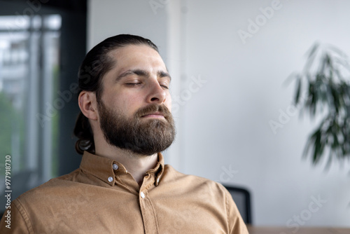 Professional man practicing meditation in office. Embodying relaxation and mindfulness, he takes a momentary break from work. Closed eyes convey peaceful mindset, promoting stress relief