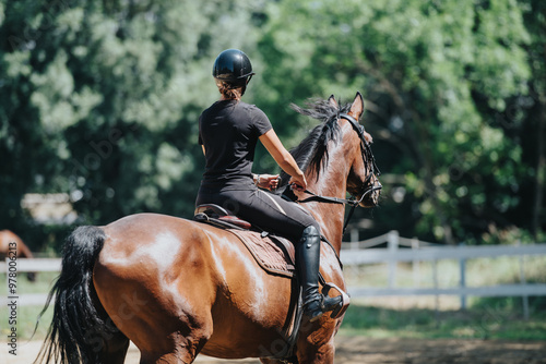 Woman riding a horse in an outdoor equestrian arena, enjoying a sunny day surrounded by nature.