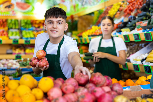 Young salesman proposing pomegranate, offering fresh fruits in supermarket