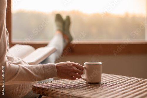 person relaxing at home reading a book and drinking a cup of hot tea 