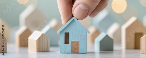 A hand placing a blue model house among smaller wooden houses, symbolizing home selection and real estate concepts.