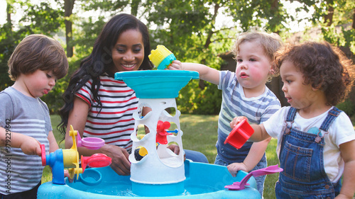 Mother And Young Children Playing With Water Table In Garden