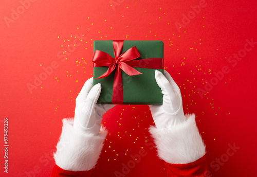 Santa Claus hands holding a beautifully wrapped green gift box with a red ribbon against a festive red background for Christmas celebration