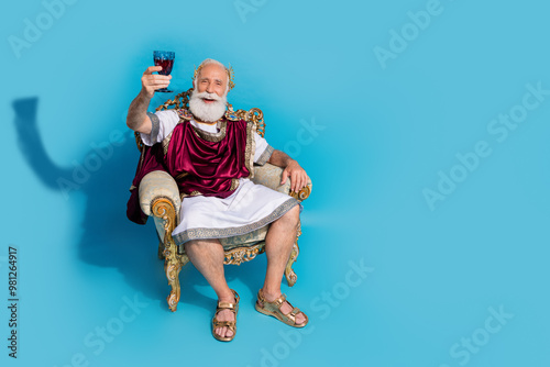 Full body portrait of rich wealthy ancient roman citizen sit throne hold wine glass empty space isolated on blue color background