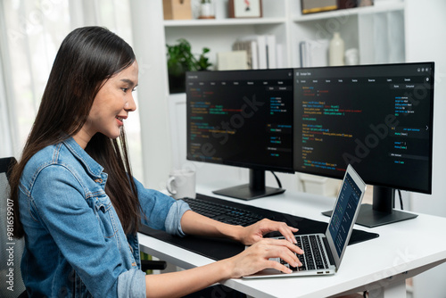 Smiling young Asian in IT developer creating with typing online information on laptop with coding program data of application, wearing jeans shirt. surrounded by safety analysis two screen. Stratagem.