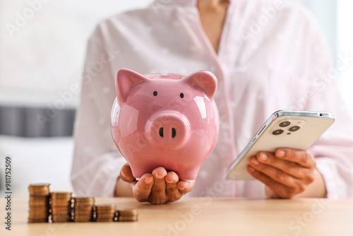 Woman with piggy bank and smartphone at table indoors, closeup