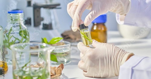 A scientist carefully examines a small vial filled with a yellowish liquid and contains a small piece of green plant. The image captures scientific exploration in lab background.