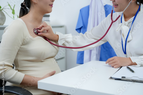 Female obstetrician listening to the chest of Asian pregnant woman with stethoscope. portrays prenatal care, doctor-patient interaction, focusing on health, well-being, and preparation for childbirth.