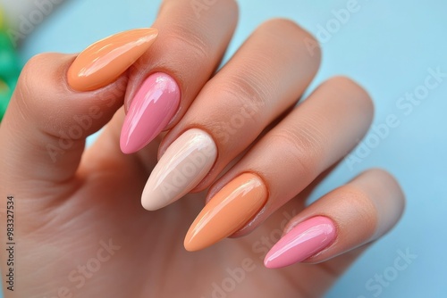 Close-up of a hand with long almond-shaped nails painted in shades of peach, pink, and beige.