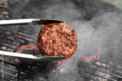 Kotlet, burger wołowy grillowany z bliska. Wokół dym unoszacy się nad żarem 