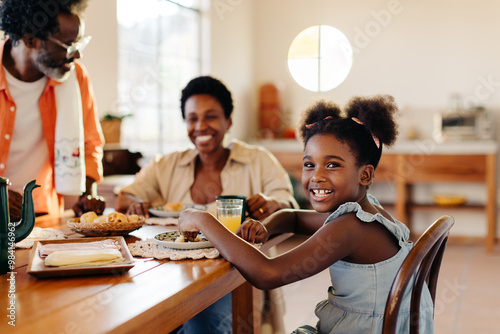 Afro-brazilian girl enjoying a cheese bread rolls breakfast with her parents at home