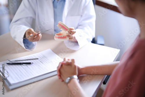 Asian dentist doctor women holding model of human jaws with teeth explaining about oral dental treatments to female patient while examination teeth and discussion about dental health in dental clinic