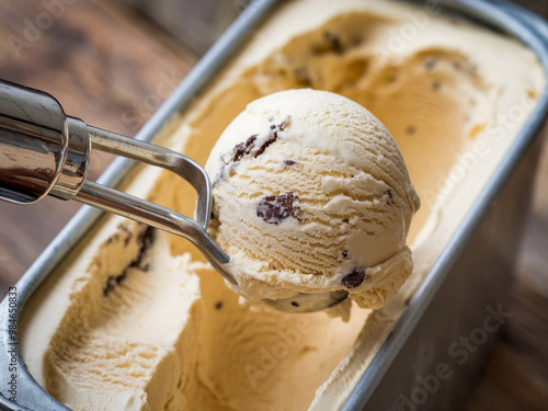 A photo of a close-up view of vanilla ice cream being scooped out of a container. The ice cream is soft and creamy, with a light brown hue.