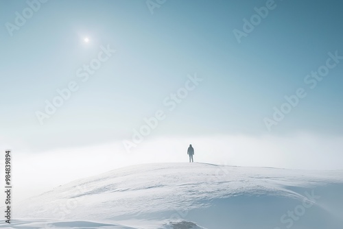 A lone person stands atop a snow-covered hill, gazing at the bright sky in the vast winter landscape.