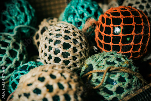 Close-up of a collection of vintage fishing floats enclosed in colorful netting. This image highlights the rustic charm and nautical theme, ideal for home decor inspiration, seaside businesses