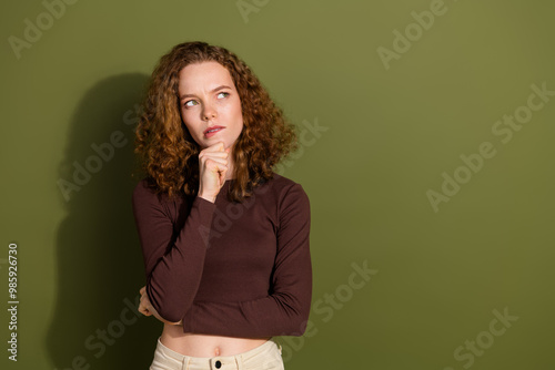 Photo of doubtful unsure girl wear brown shirt arm chin looking empty space isolated green color background