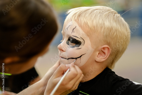 Child doing outdoor skeleton face painting in preparation for carnival. Outdoor Halloween party. Activity for kids