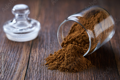 cinnamon powder poured out of a storage jar on a dark wooden table.