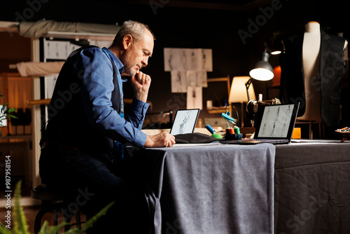 Elderly fashion designer creating refined premium quality outfit, looking online for inspiration. Senior couturier trying to come up with ideas for upcoming bespoken sartorial collection