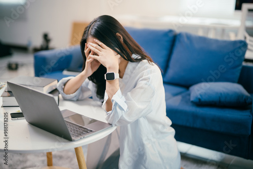 Young asian woman is experiencing stress and burnout while working from her home office. She is holding her head in her hands, feeling overwhelmed by the demands of her work