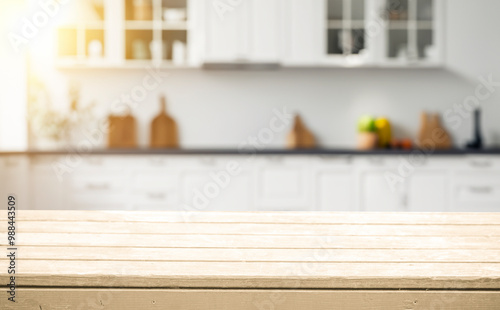 Empty wooden countertop in a bright kitchen with white cabinets and sunbeams.