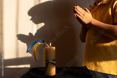 burning candle, two ears of wheat, painted yellow-blue against of shadow of child with his hands folded in prayer. tragic page in Ukrainian history . Day of Remembrance of Holodomor Victims in Ukraine